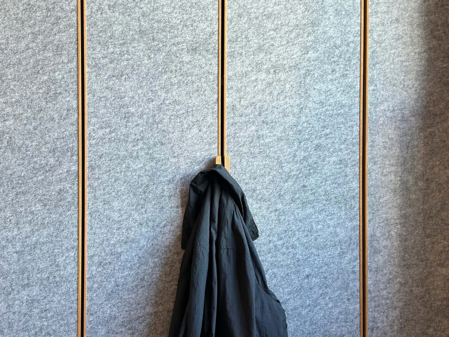 A dark coat on a hook against a felt panel.