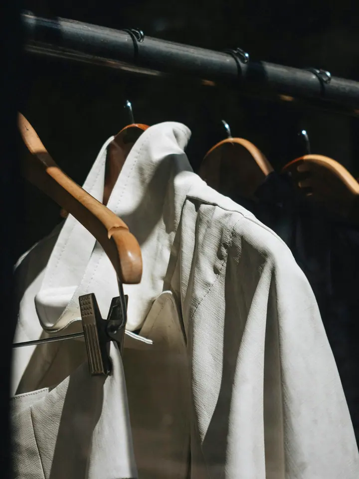 Shirts on wooden hangers, lit hard from one side against a dark ground.