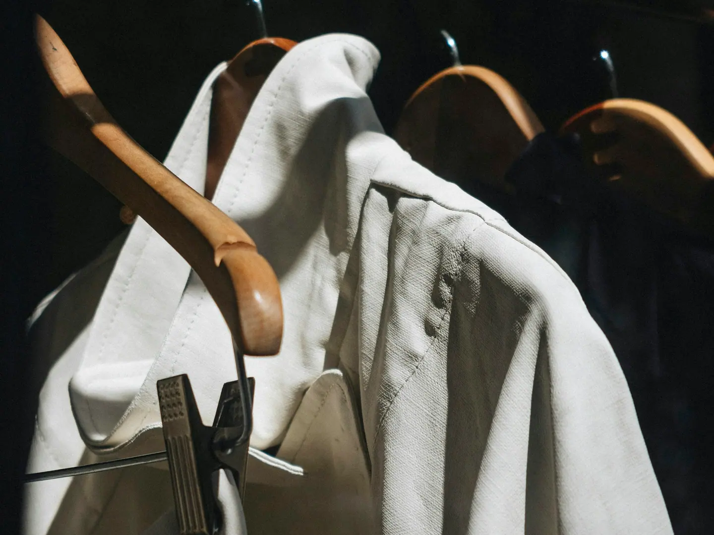 Shirts on wooden hangers, lit hard from one side against a dark ground.