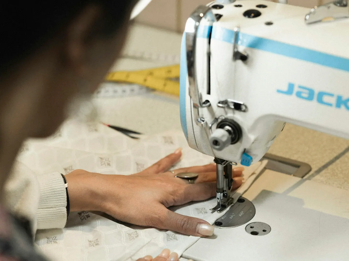 Hands feeding cloth through a flatbed machine.