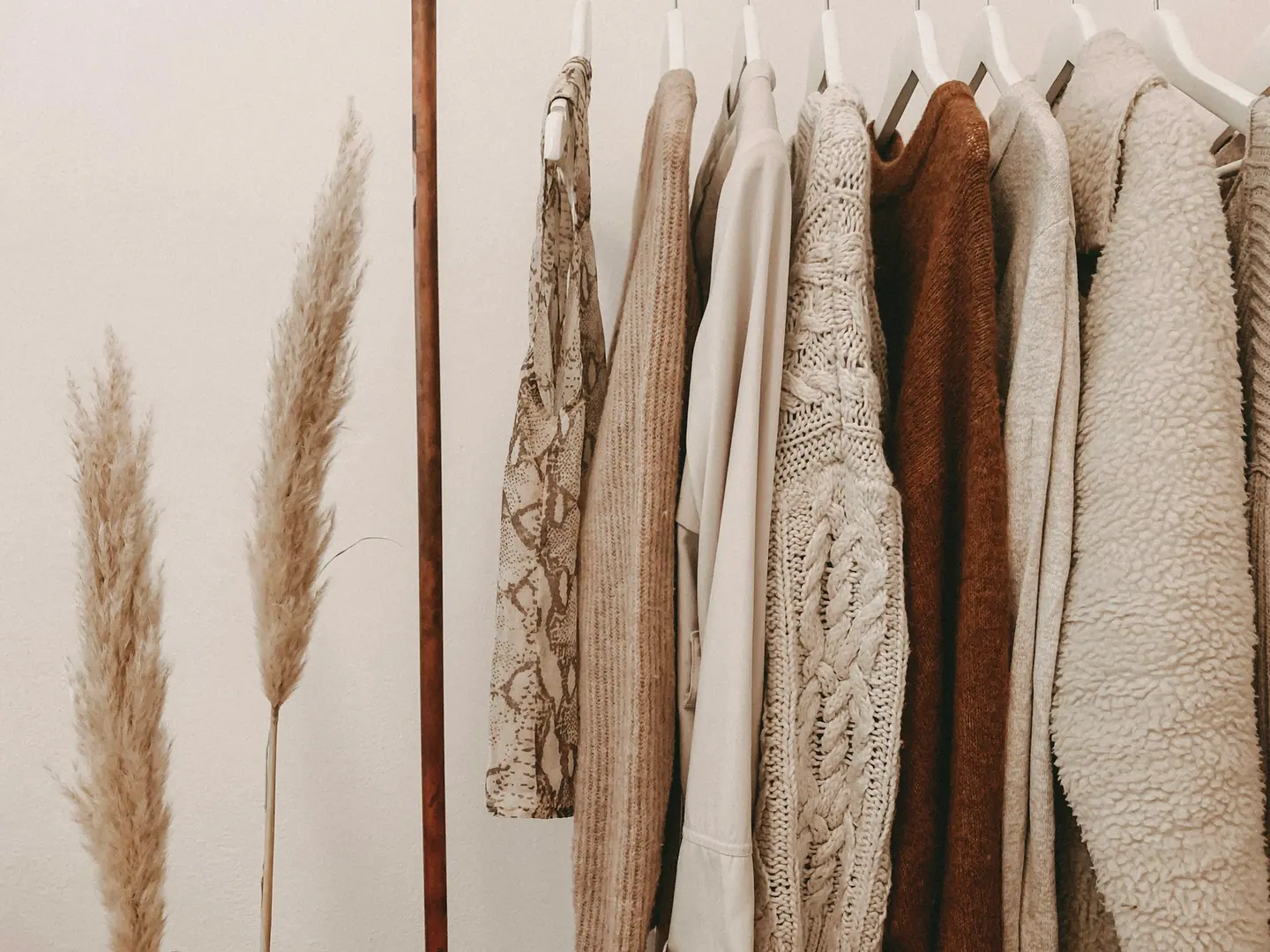 Neutrals and knitwear on a rail beside dried grasses.