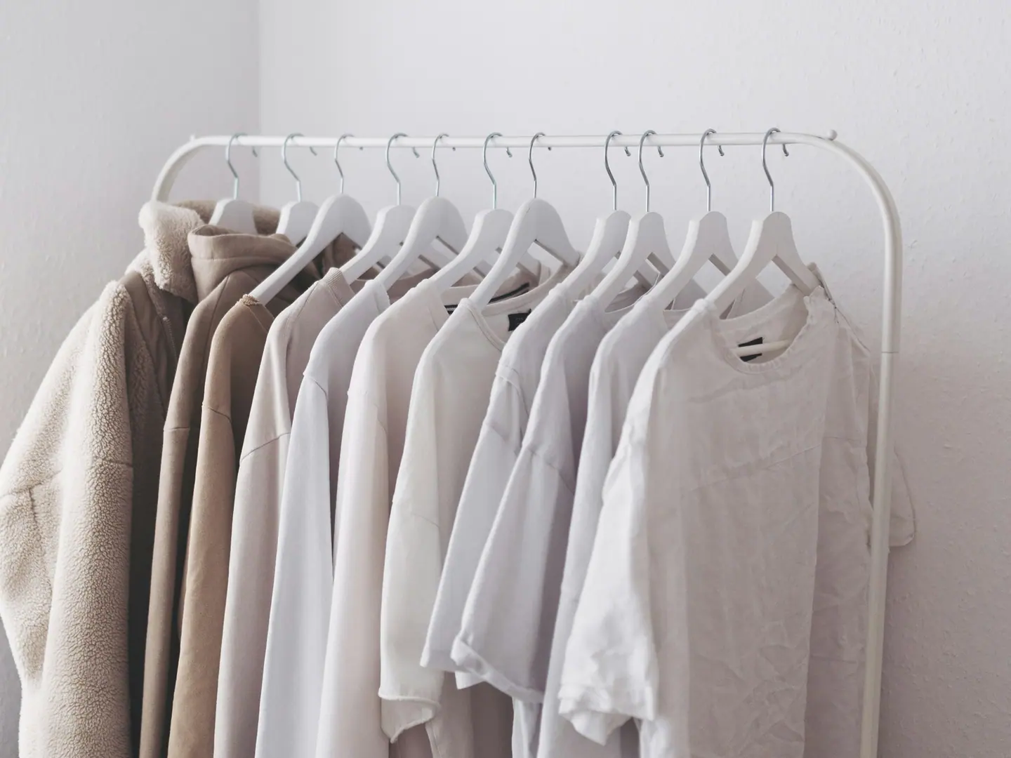 A rail of undyed linen shirts against a white wall.