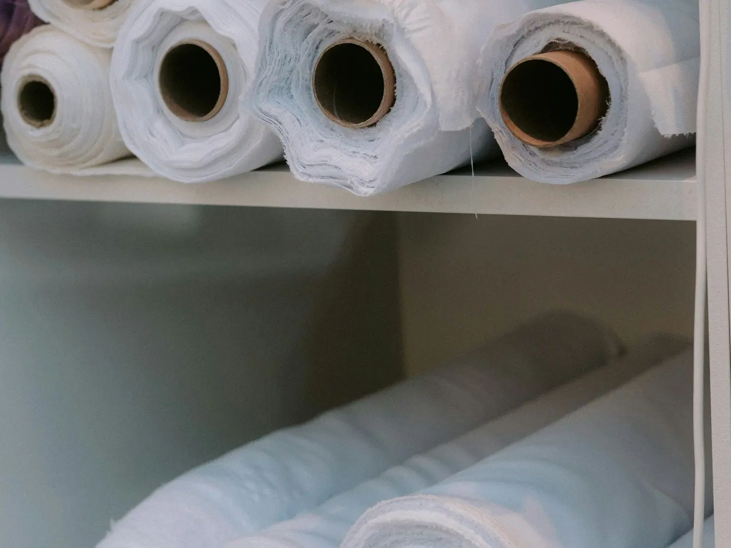 Rolls of undyed cloth on a shelf, relaxing before they are cut.
