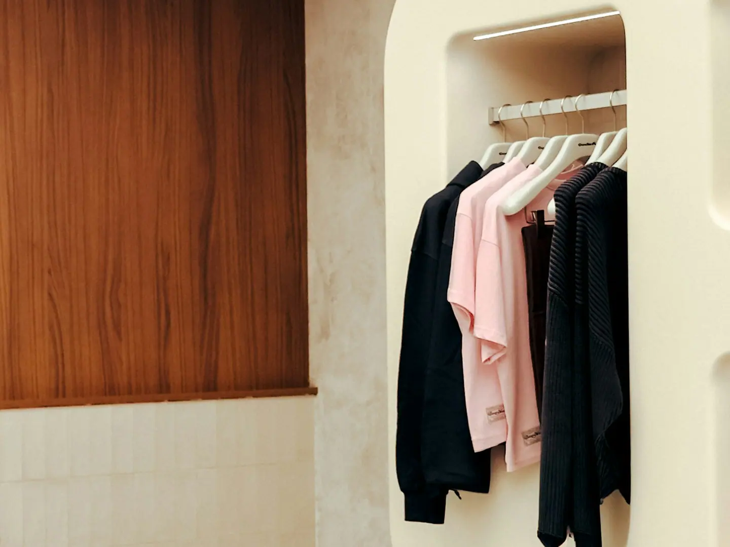 Curved cream shelving in the shop, holding folded pieces and a row of hangers.