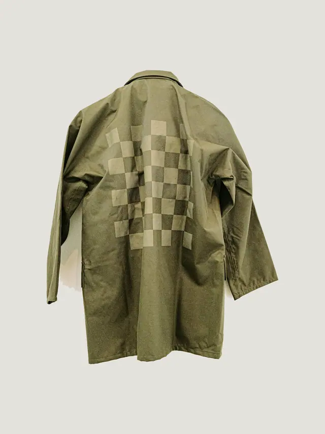 The Field Coat in olive cotton canvas, unlined, laid flat on grey pattern paper.